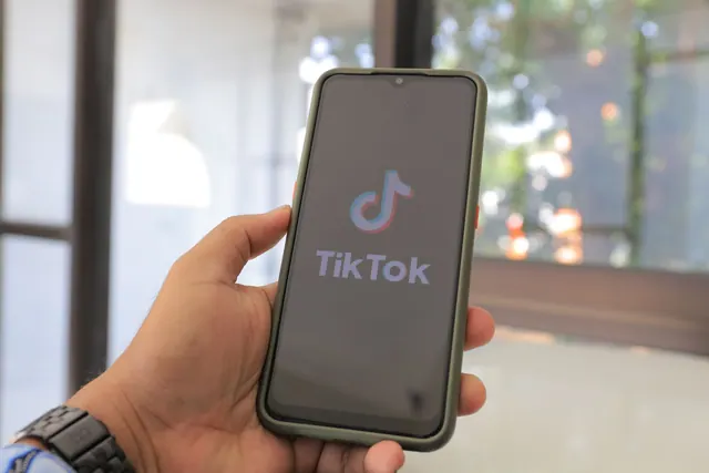 Close-up of a hand holding a smartphone with the TikTok app on screen in a bright indoor setting. Platform trends guide: history, examples and current context