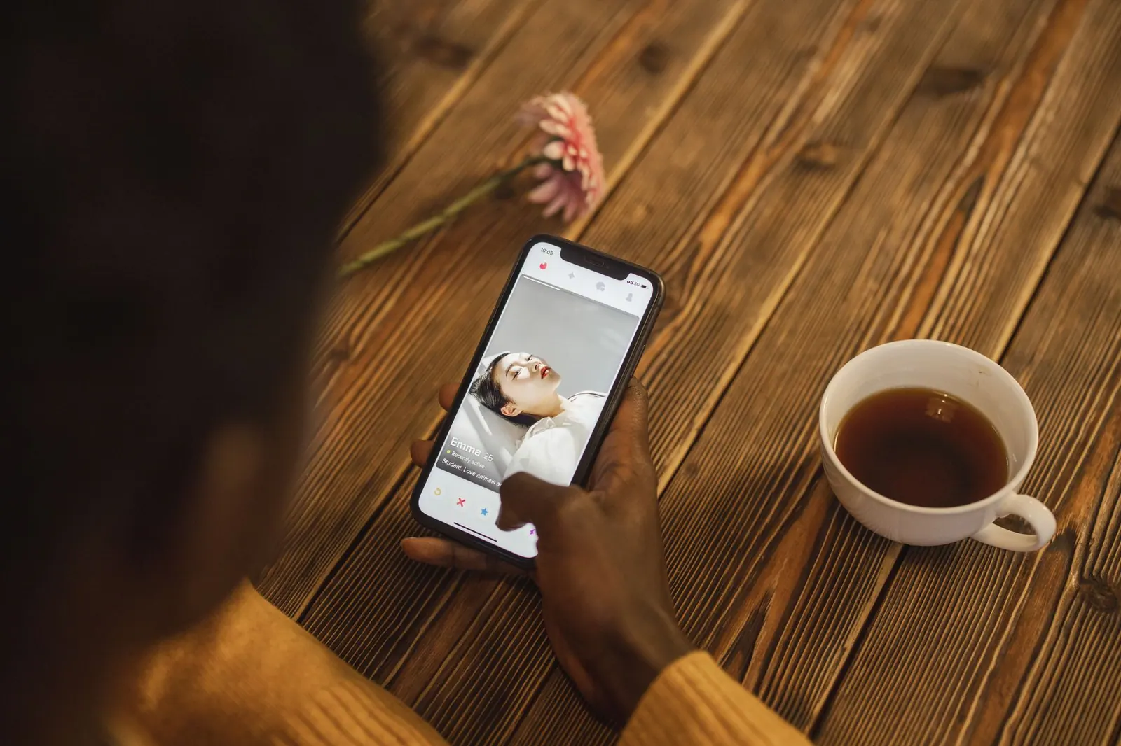An individual using a dating app on a smartphone with a cup of tea nearby on a wooden table. The arithmetic of a viral trend hasn't changed much heading into 2027